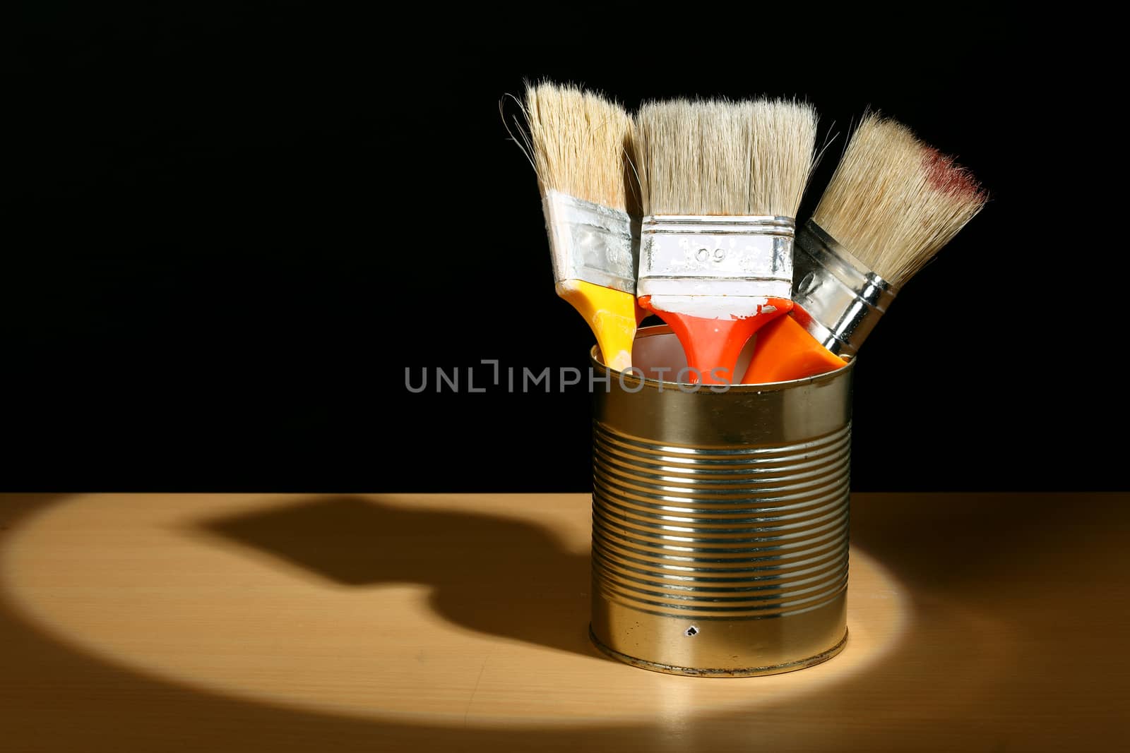 Three clean paint brushes in tin can in the spotlight.