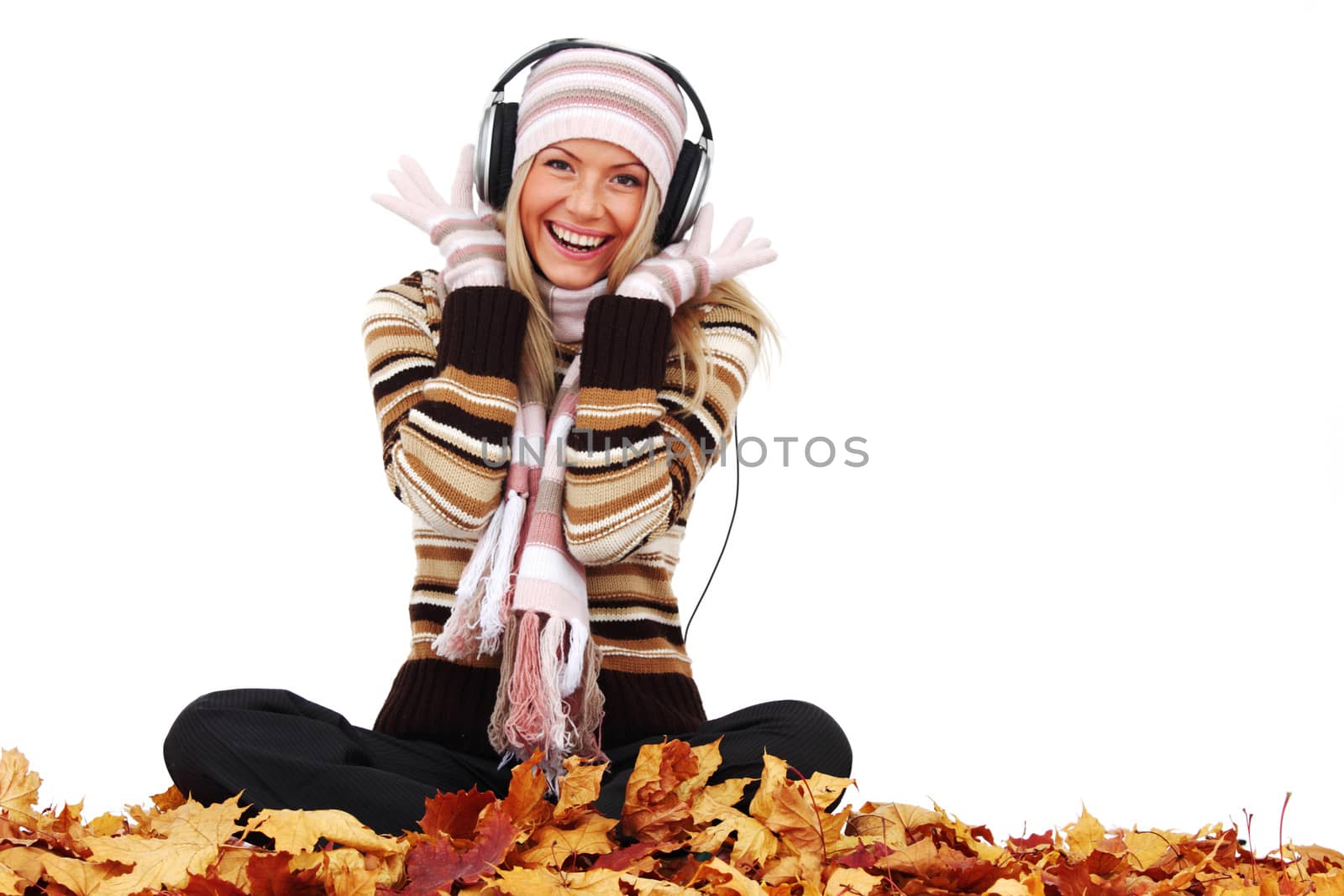 Beautiful young woman listening music sitting on autumn leaves, isolated on white