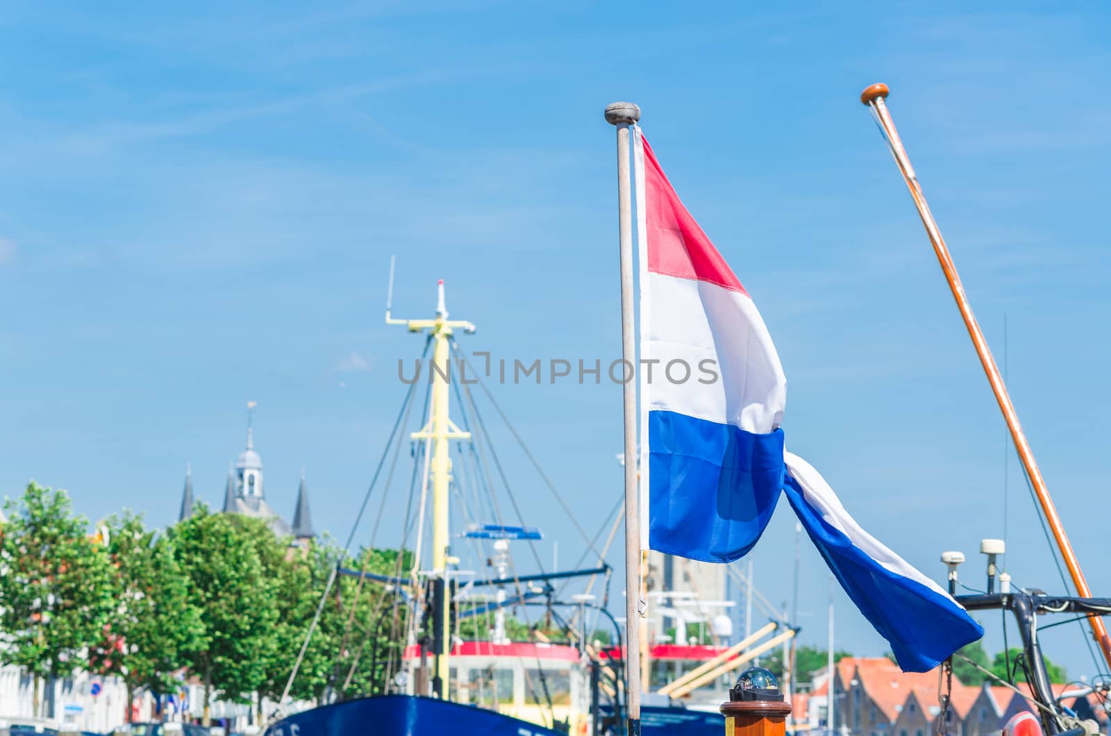 Looking in a dutch Marina, Mast with flag of the Netherlands against blue sky.