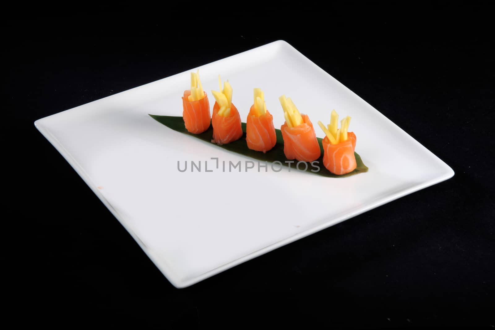 rolls of salmon on white plate, black background