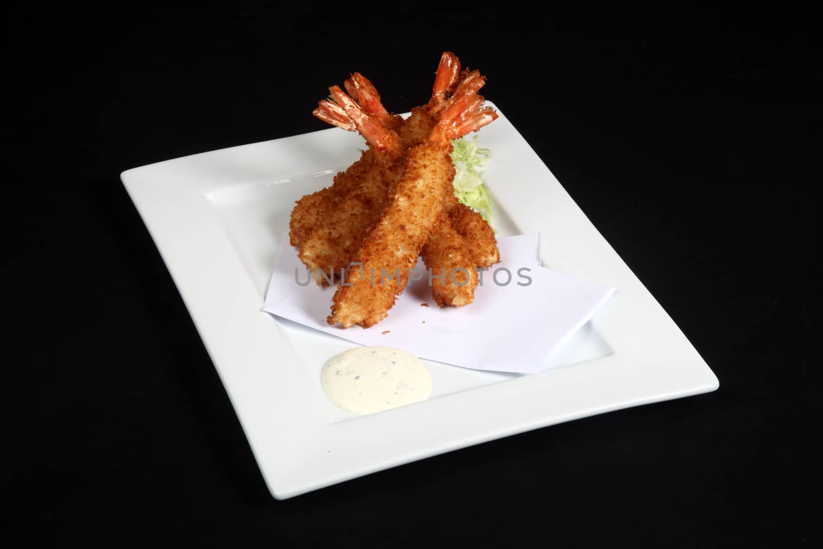 breaded prawns with vegetables and sauce in white plate on a black background