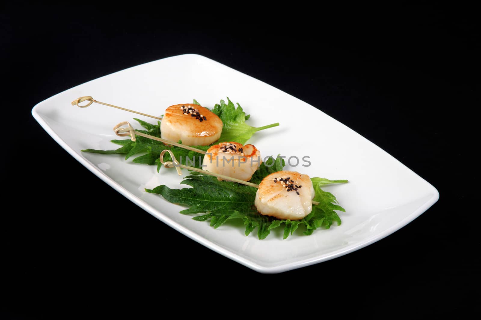 grilled scallops with vegetables on square plate on a black background
