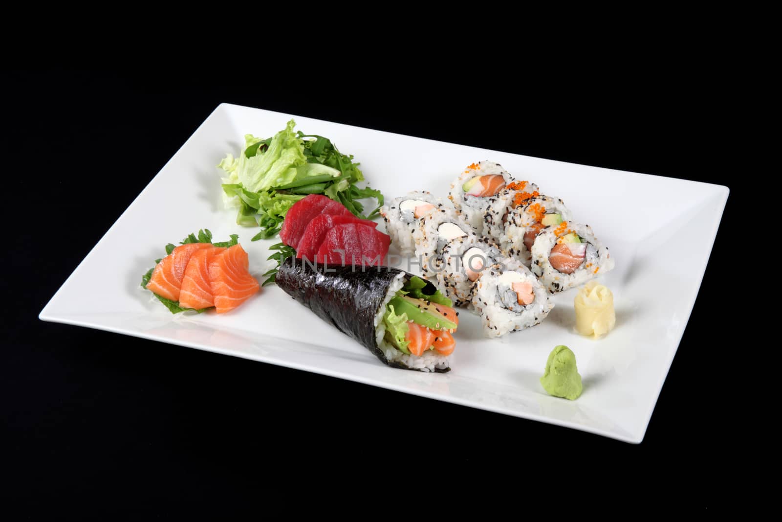 sushi and sashimi with wasabi and vegetable in white plate on a black background