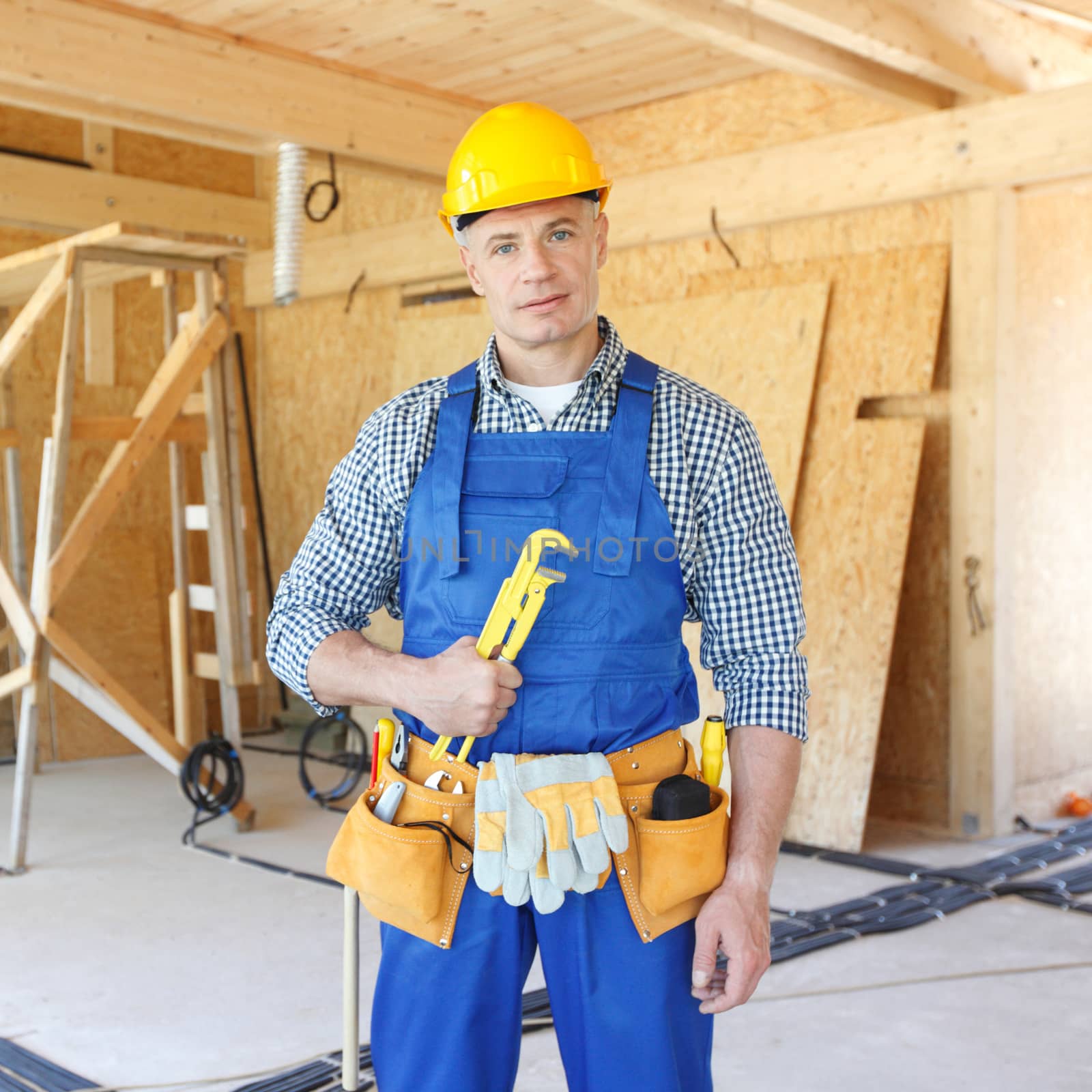 Workman with wrench inside wooden house under construction