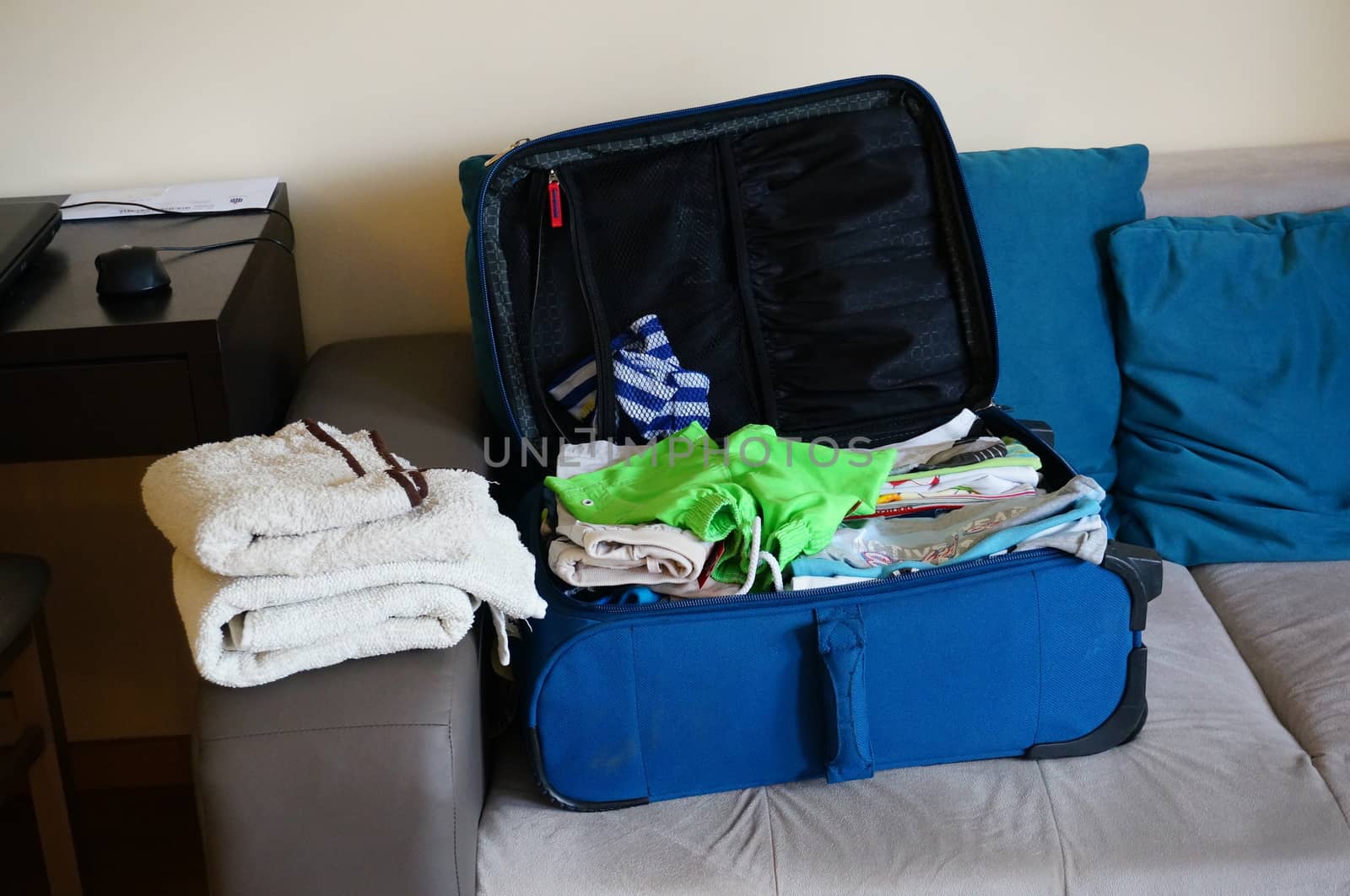 Blue suitcase full of clothes lying on sofa