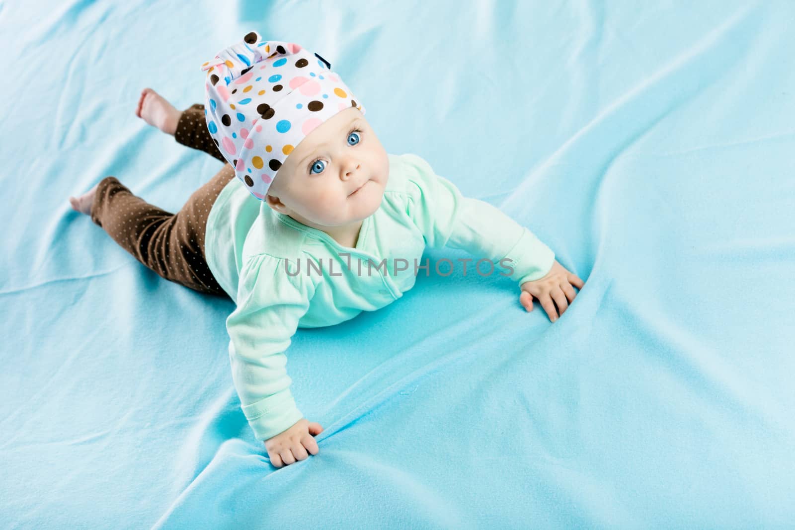 The blue-eyed baby in hat crawling on the blue coverlet
