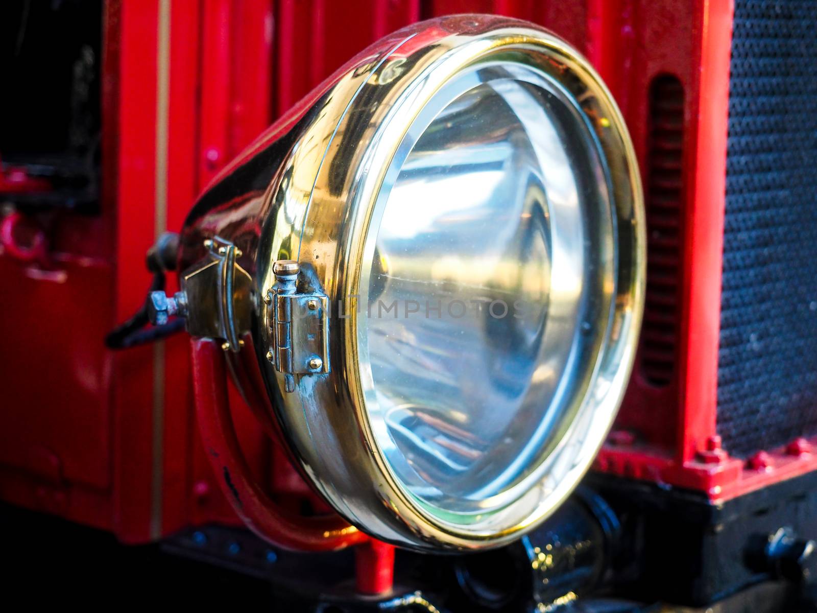 Closeup of brass headlight with glass on old red vehicle  by Arvebettum