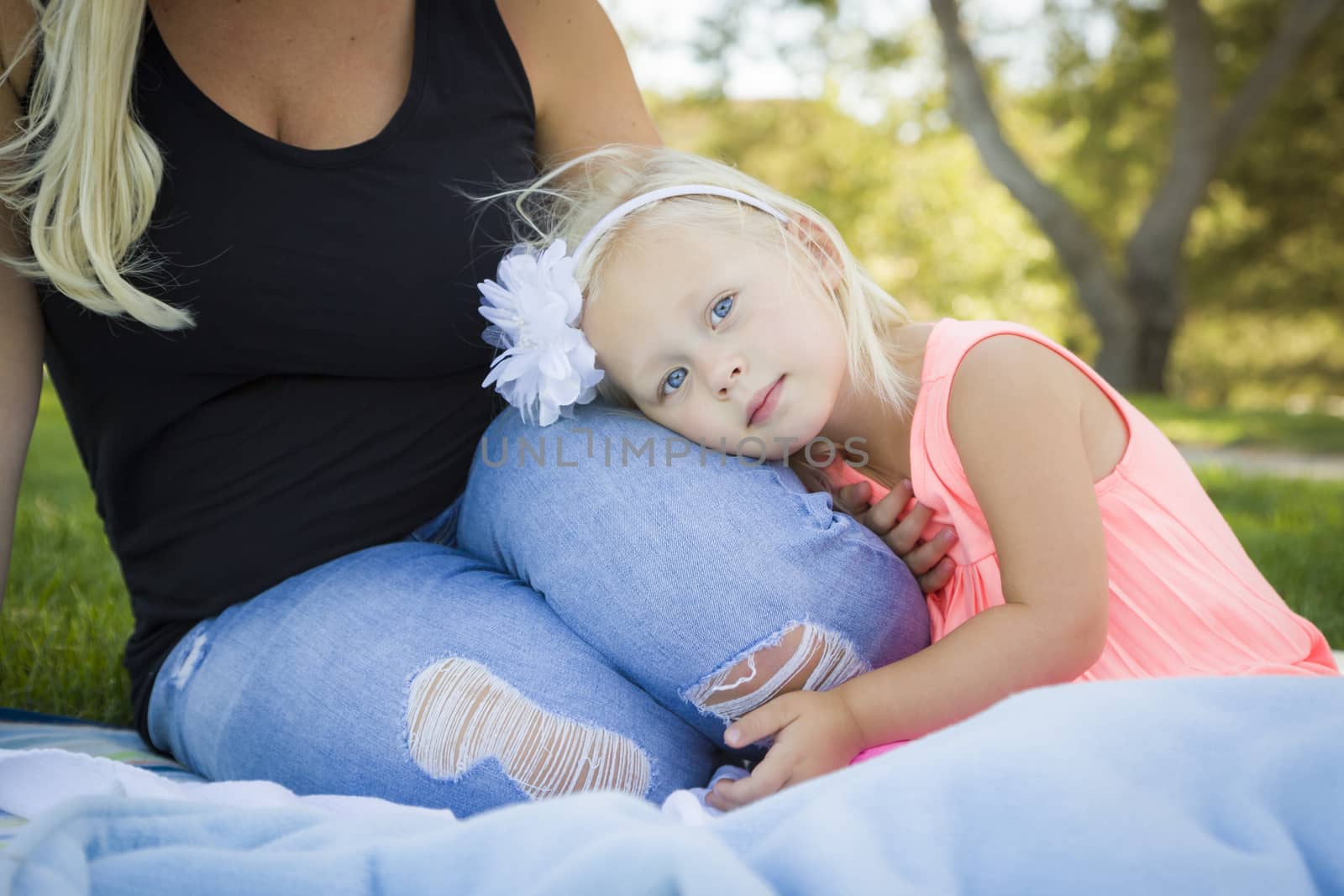 Beautiful Young Blue Eyed Girl Resting on Her Mommy's Lap Outside At the Park.