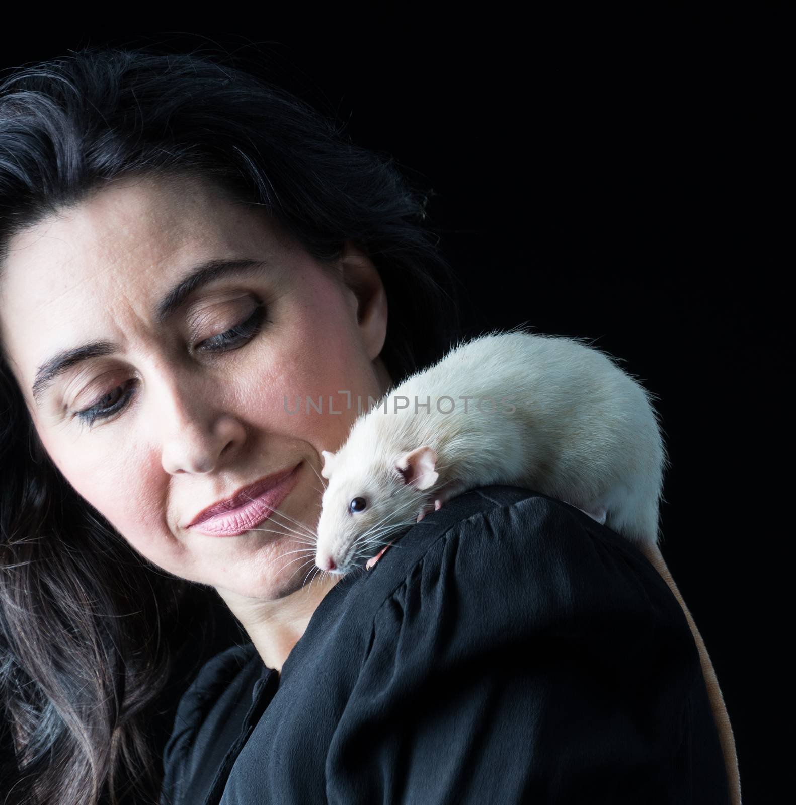 Woman in black standing in front of a black backdrop with a white dumbo rat perched on her shoulder.