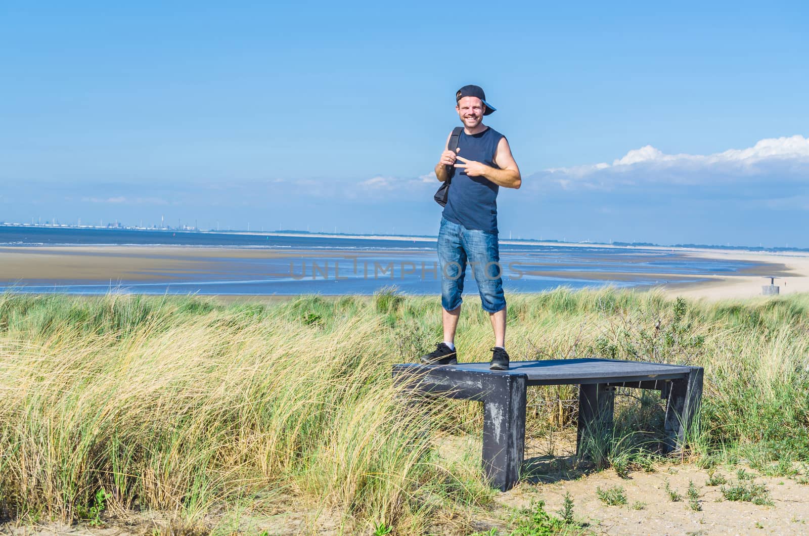 Young man in the summer with 3/4 jeans. Standing on an observation deck on the beach. Teenager relaxing and enjoying rest on holidays.

