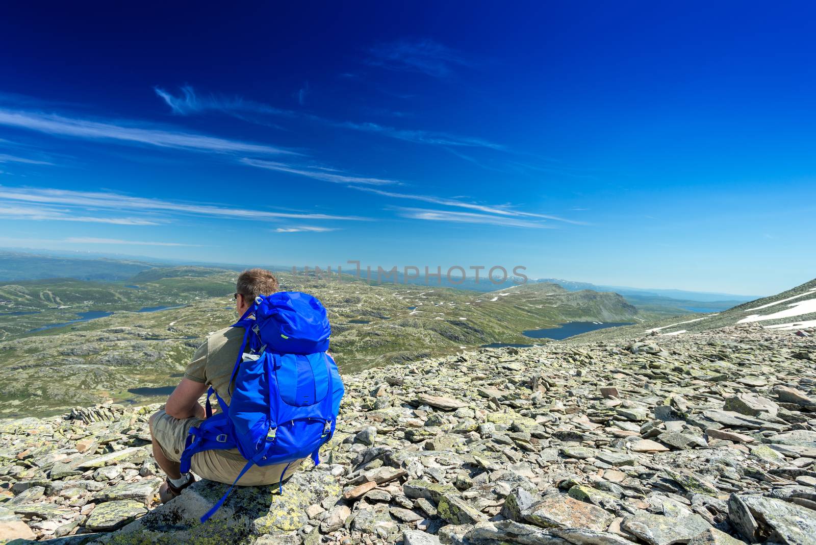 Hiker with big traveling rucksack looking forward on the mountai by Nanisimova