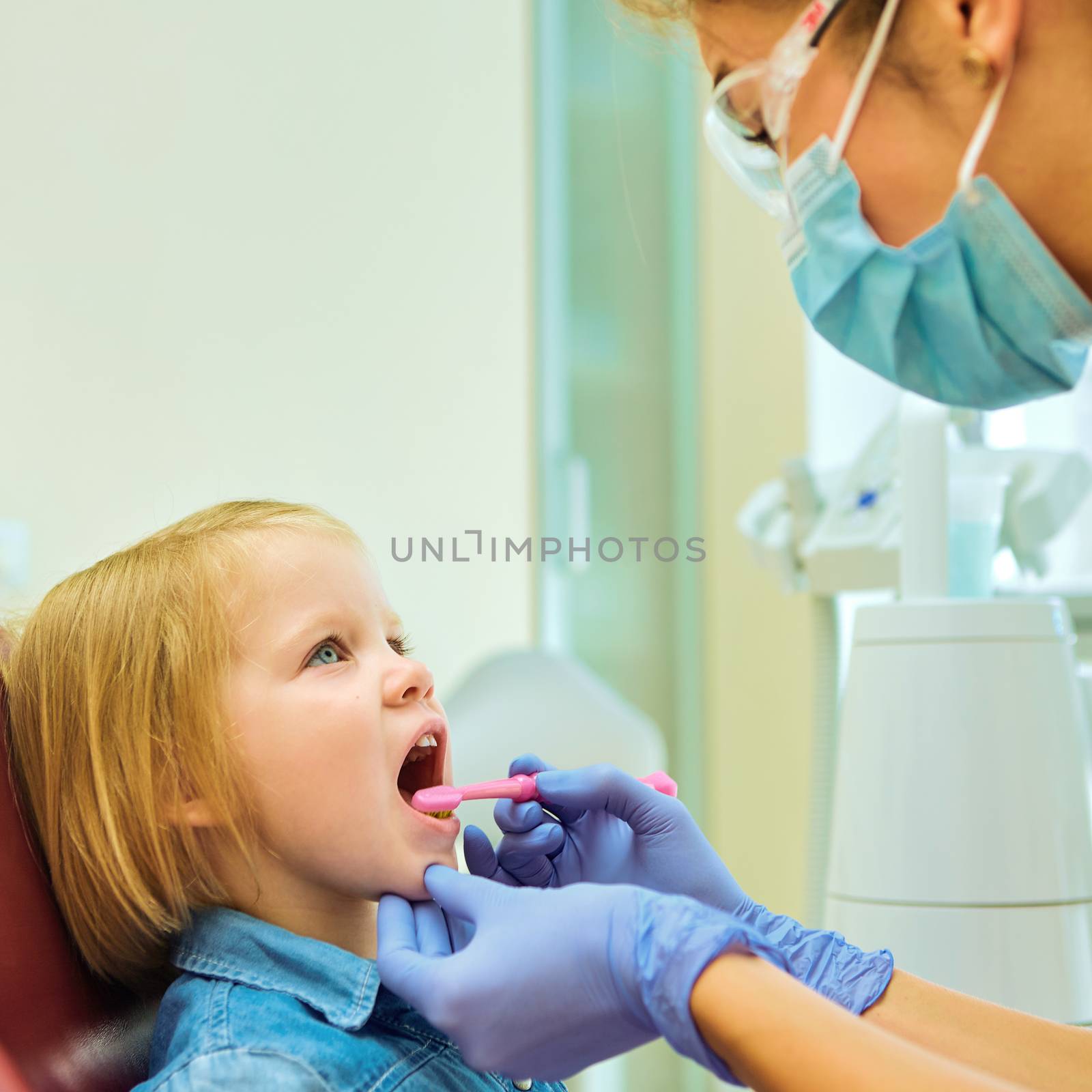 Little patient at the dentist office. The dentist brushes teeth to the little girl