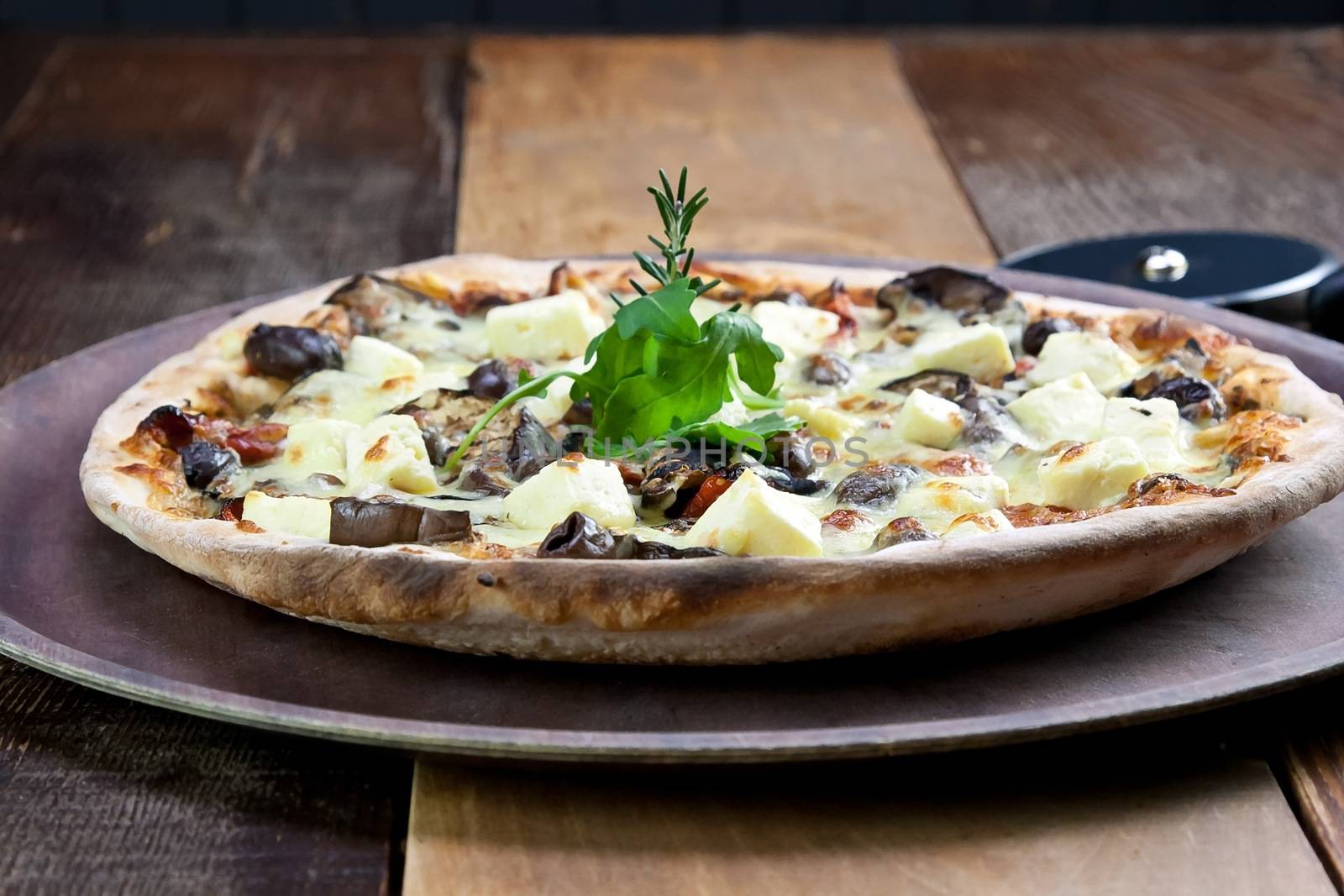 A single pizza laid out on a wooden tray on a wooden tables in a pizzeria.