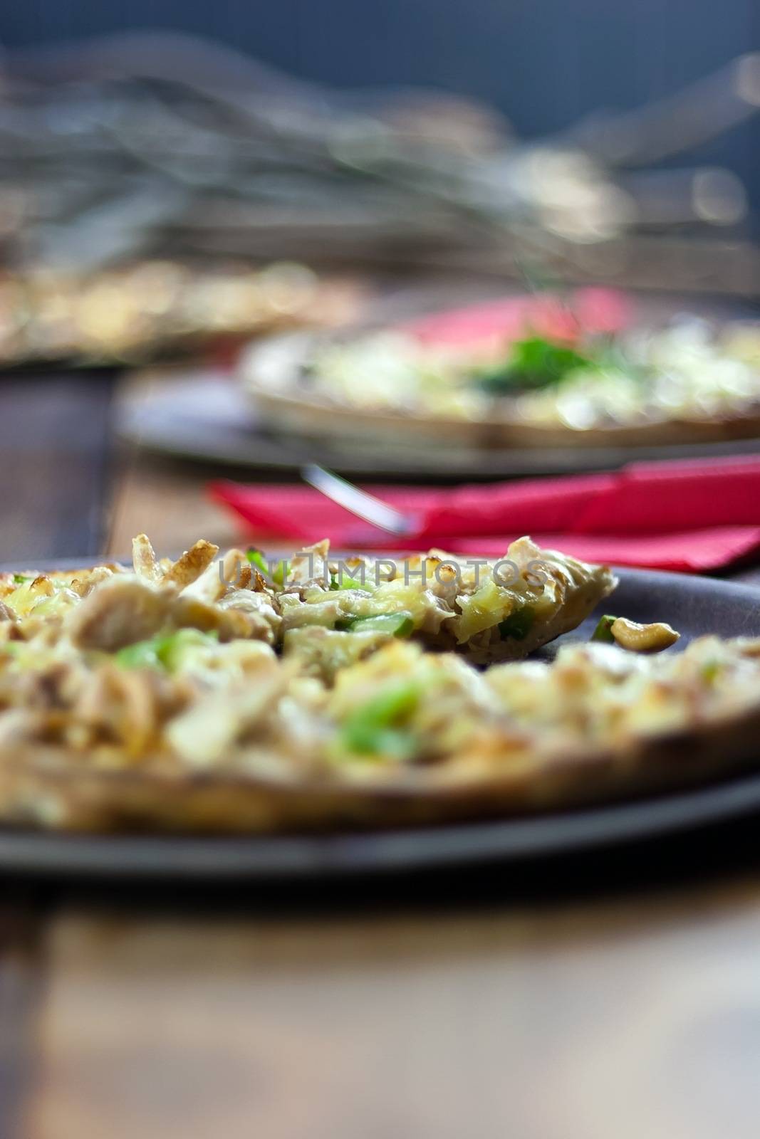 Three pizzas laid out on wooden trays on a rustic wooden table in a pizzeria.