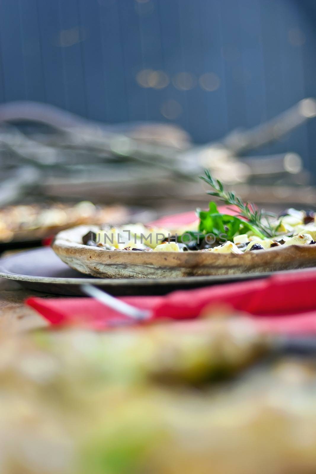 Three pizzas laid out on wooden trays on a rustic wooden table in a pizzeria.