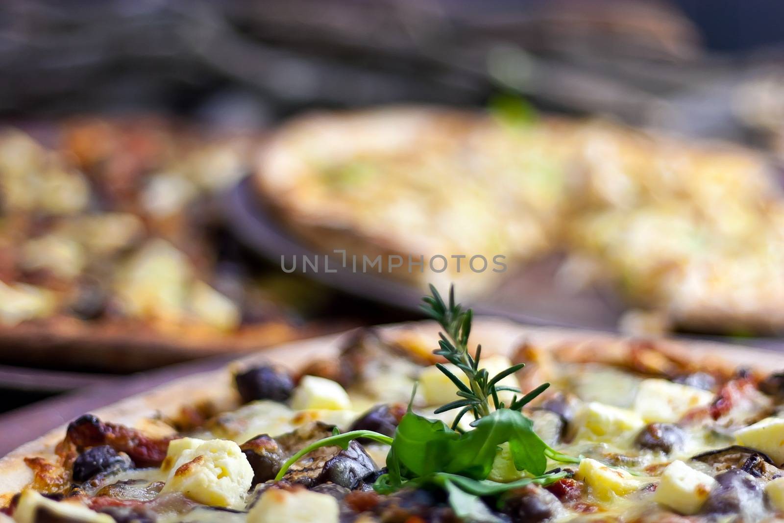 Three pizzas laid out on wooden trays on a wooden tables in a pizzeria.