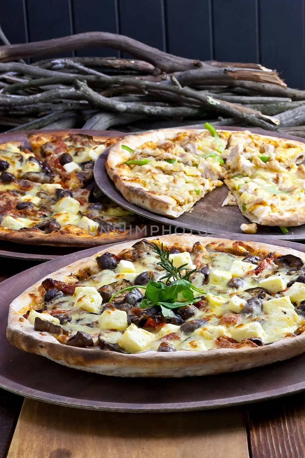  Three pizzas laid out on wooden trays on a wooden tables in a pizzeria.