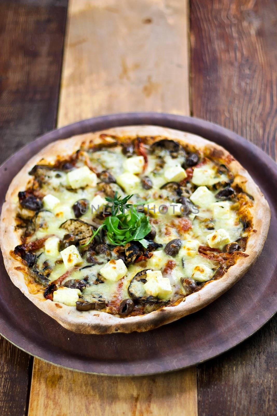 A Vegetarian pizza laid out on a wooden tray on a wooden table in a pizzeria.