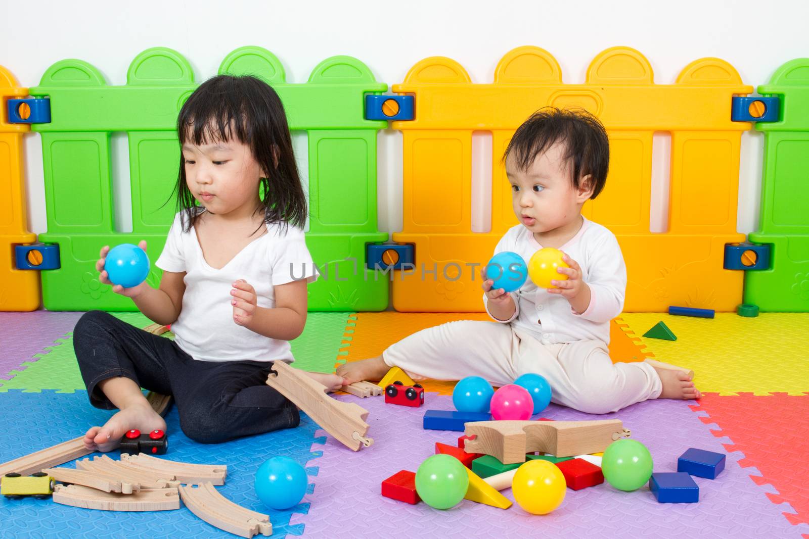 Two Asian Chinese little girls playing with blocks and toys train on the floor at kingdergarten.