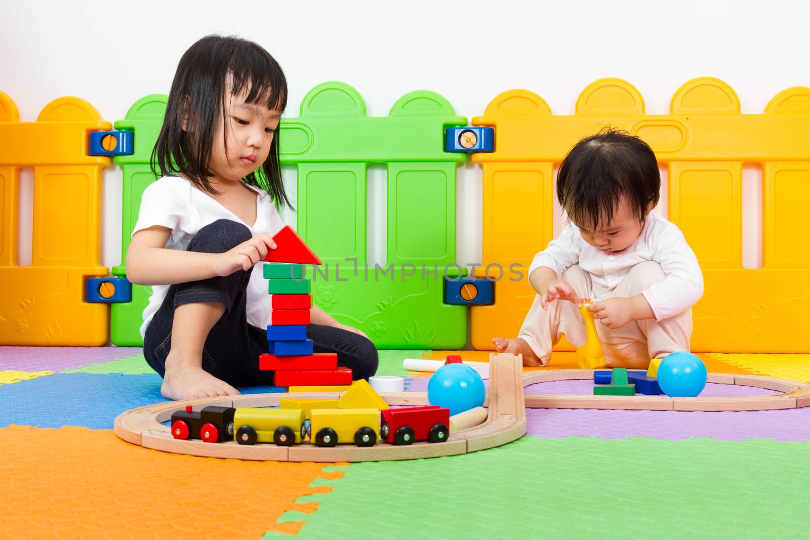 Two Asian Chinese little girls playing with blocks and toys train on the floor at kingdergarten.