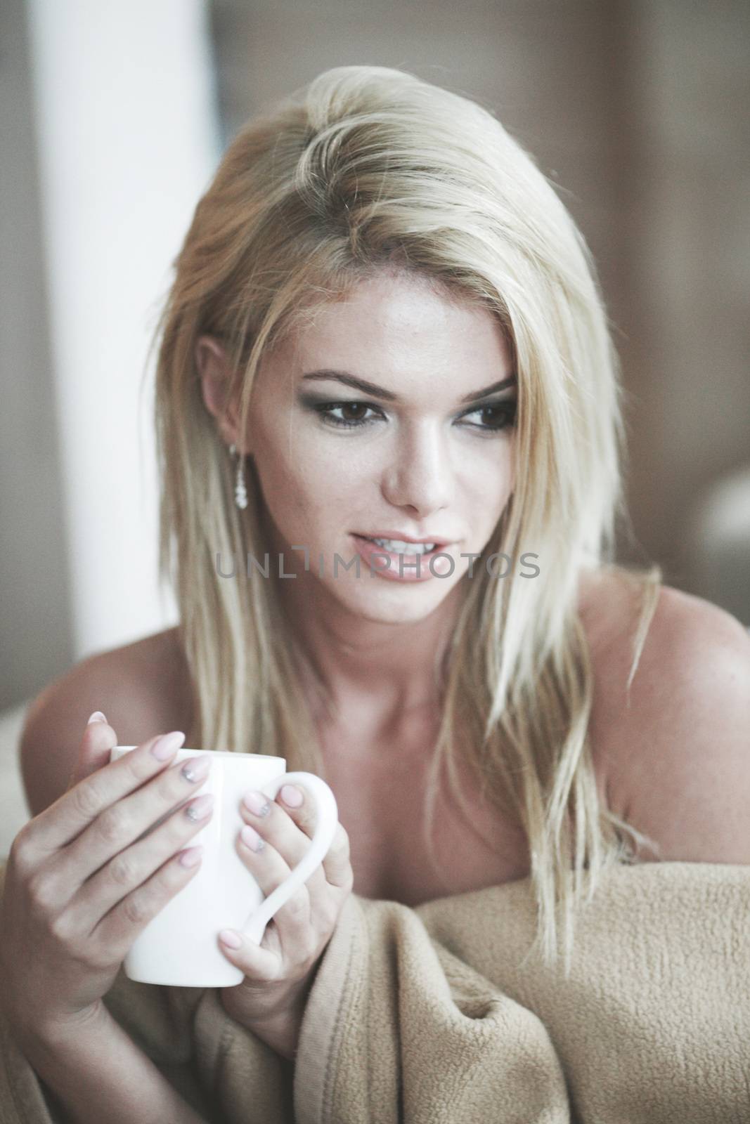 Sexy blond woman with coffee wrapped in beige blanket