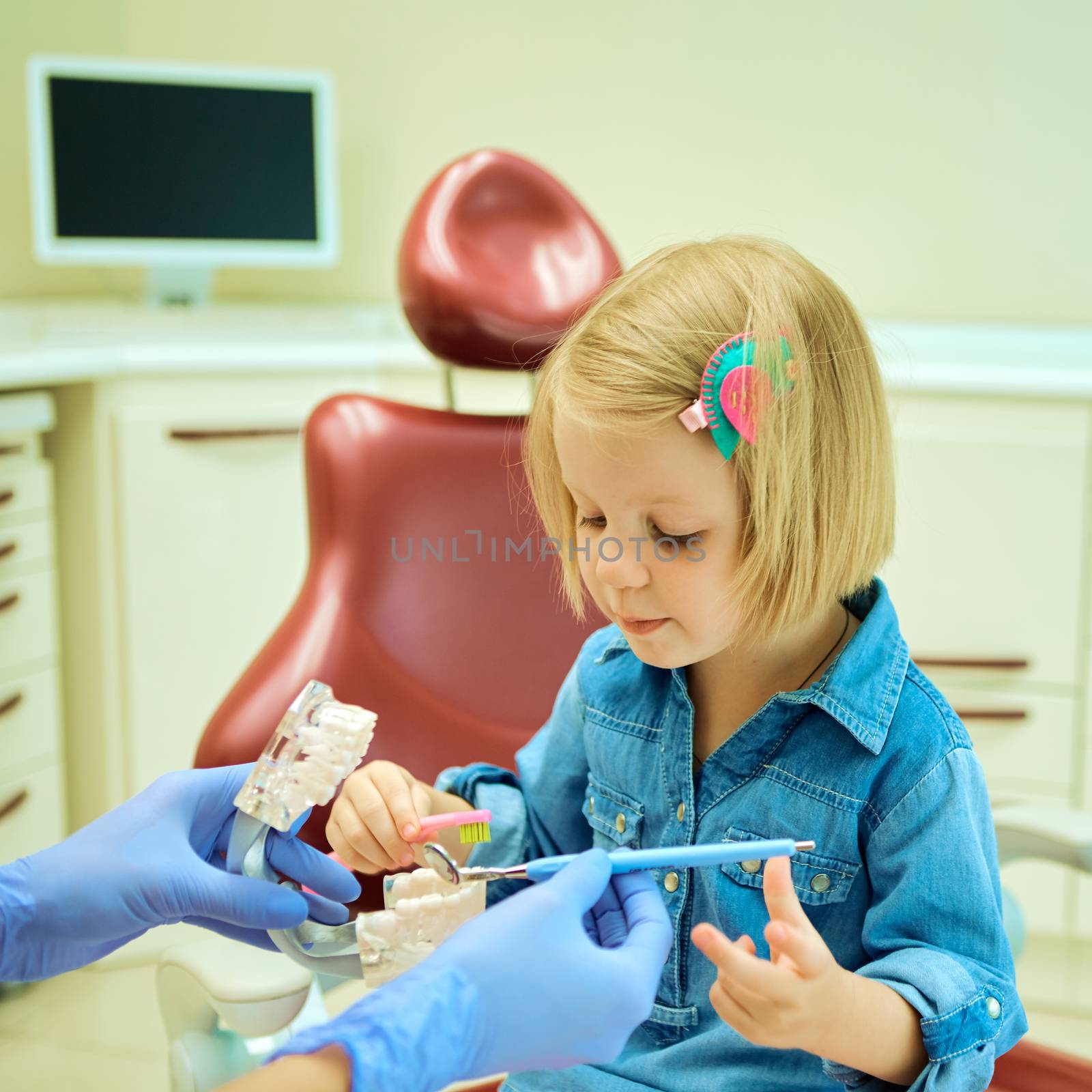 Little girl sitting in the dentists office learning to clean teeth