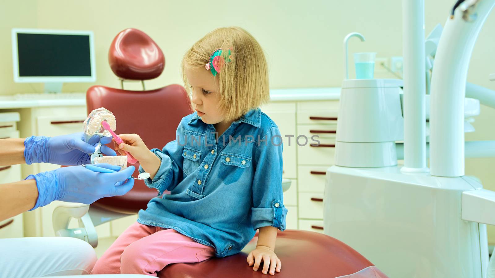 Little girl sitting in the dentists office learning to clean teeth