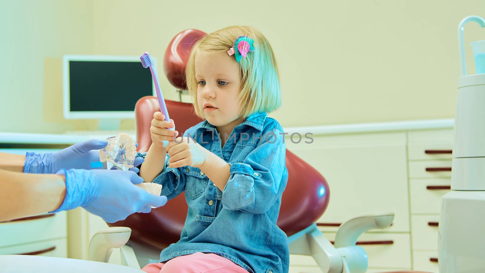 Little girl sitting in the dentists office learning to clean teeth