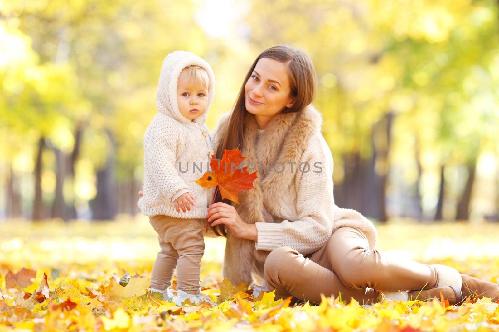 Mother and child having fun in autumn park among yellow leaves