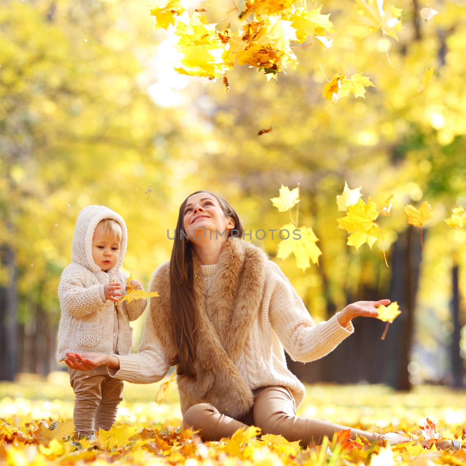 Mother and child having fun in autumn park among yellow leaves