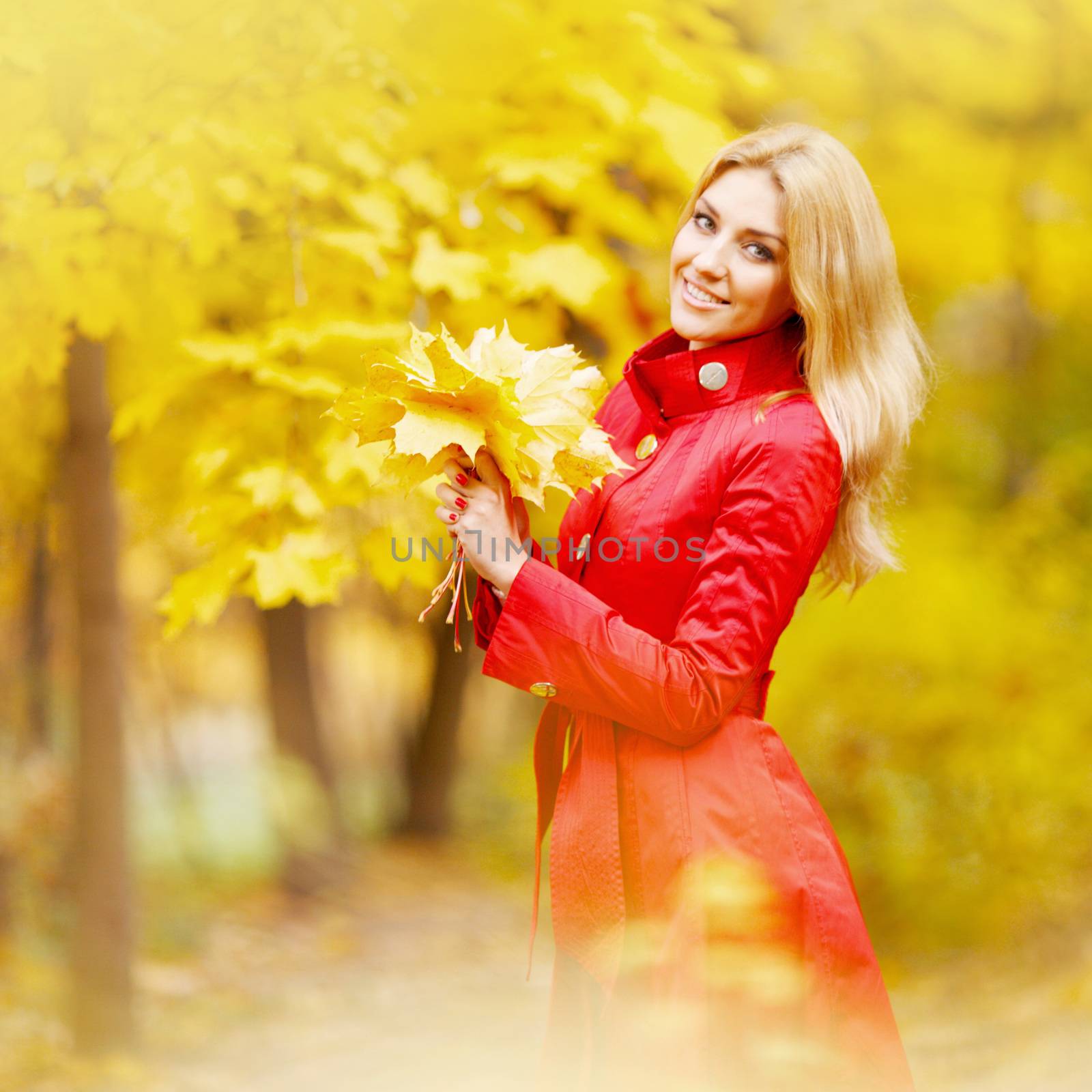 Portrait of happy woman holding in hands bunch of dry maple leaves in autumn park
