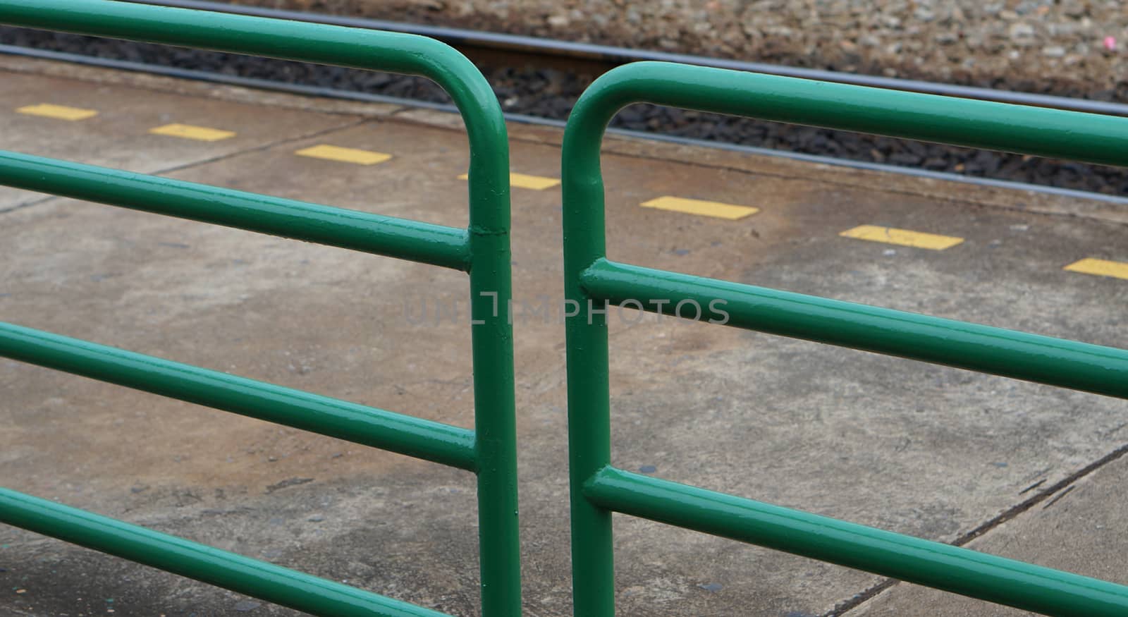 Green metal fence and yellow dash line at train station.                                