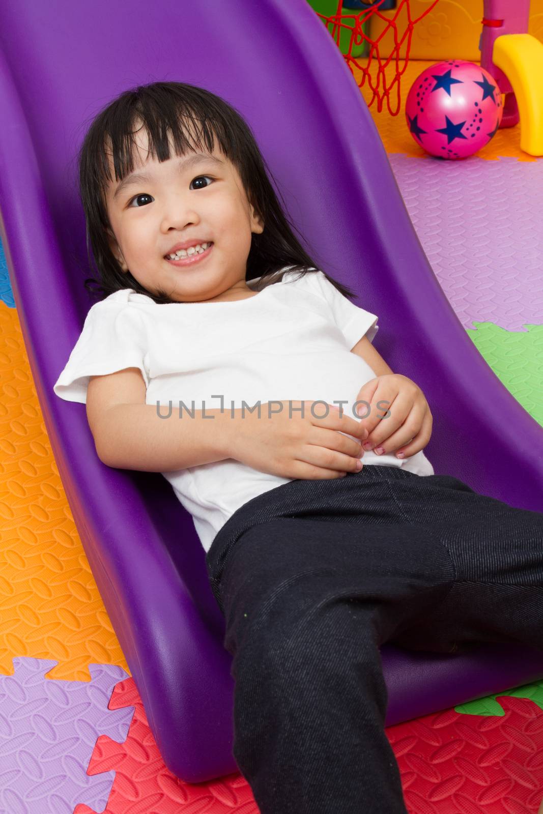 Asian Chinese little girl playing on the slide at indoor colourful playground.
