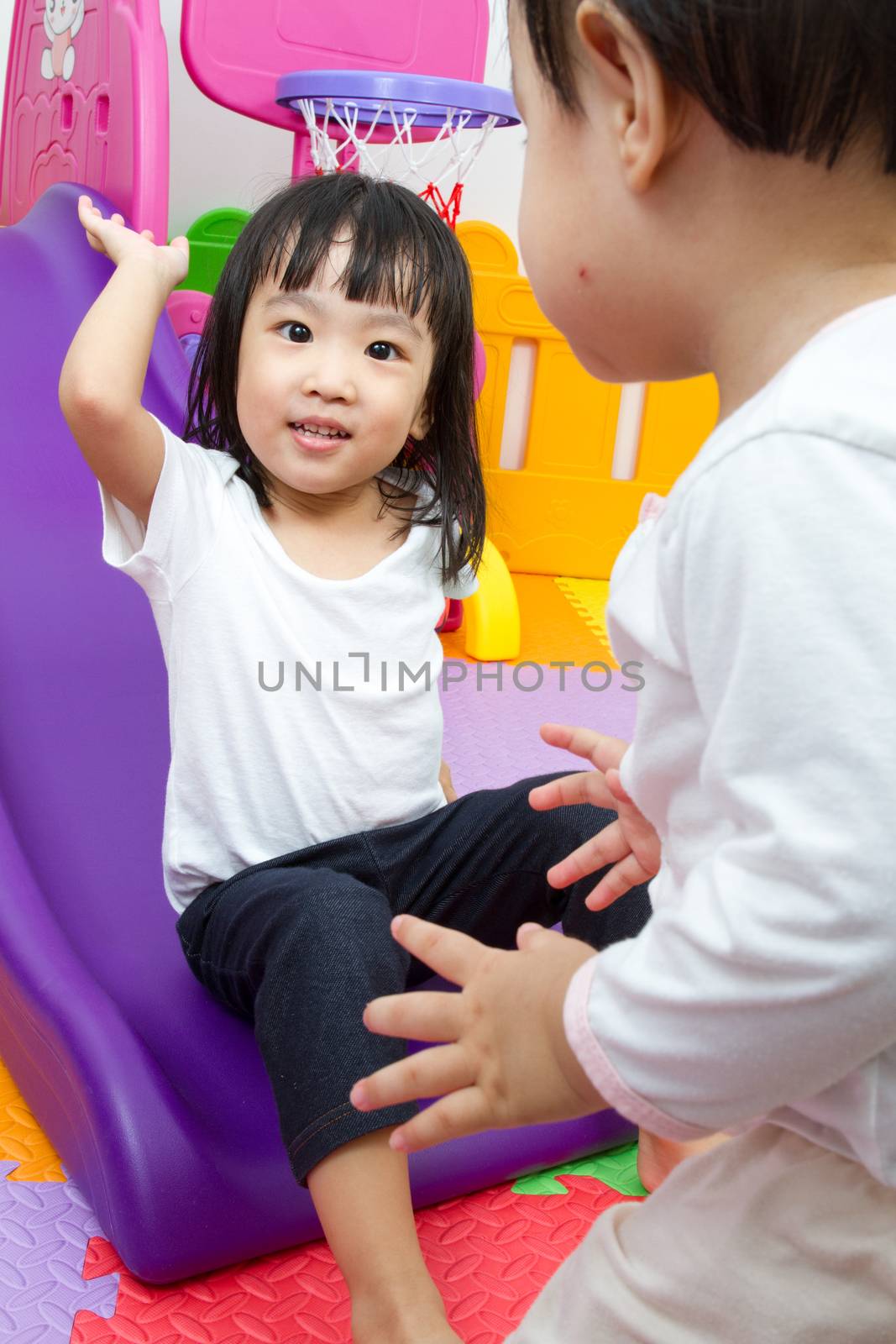 Asian Chinese little sister and brother playing on the slide at indoor colourful playground.