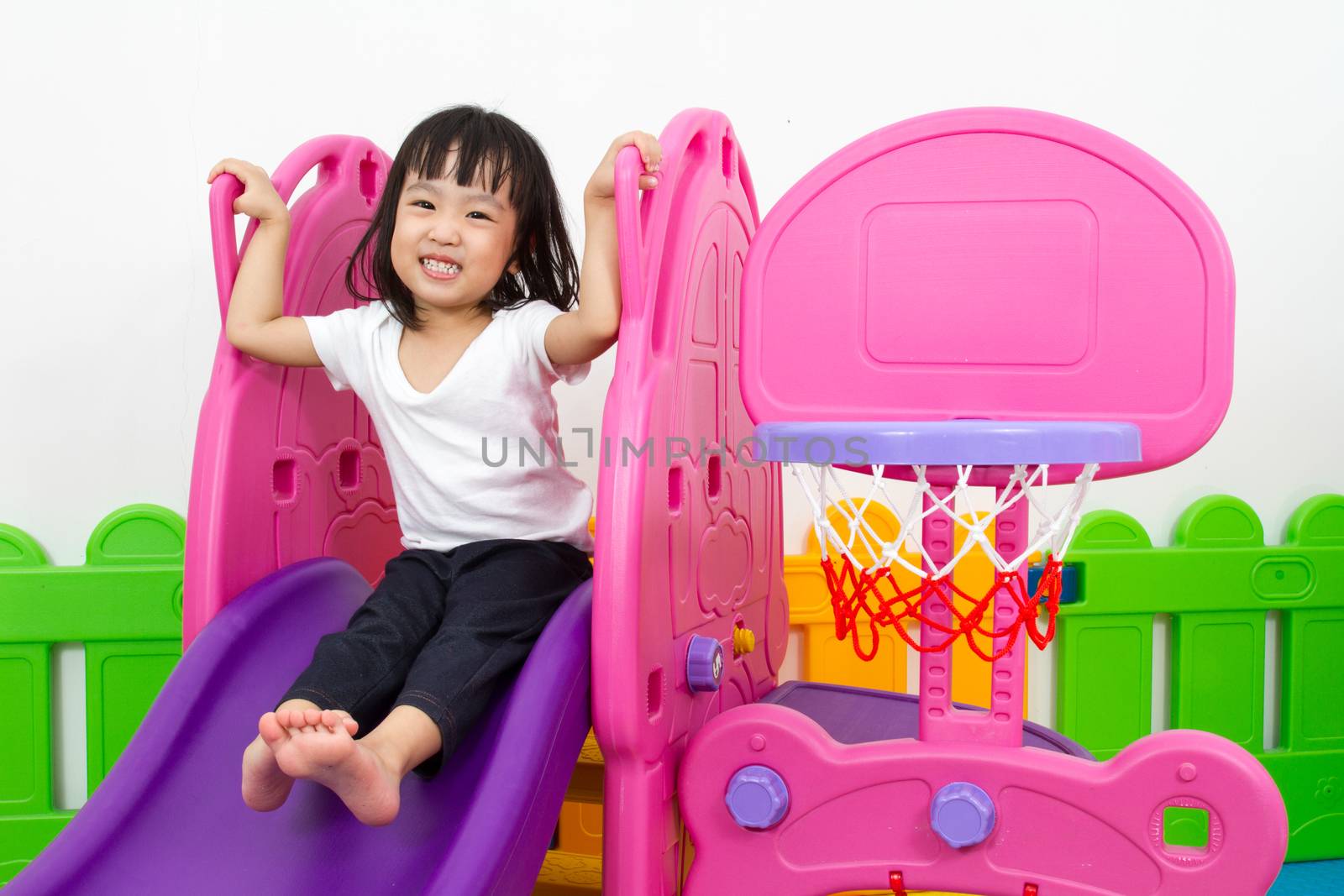 Asian Chinese little girl playing on the slide at indoor colourful playground.