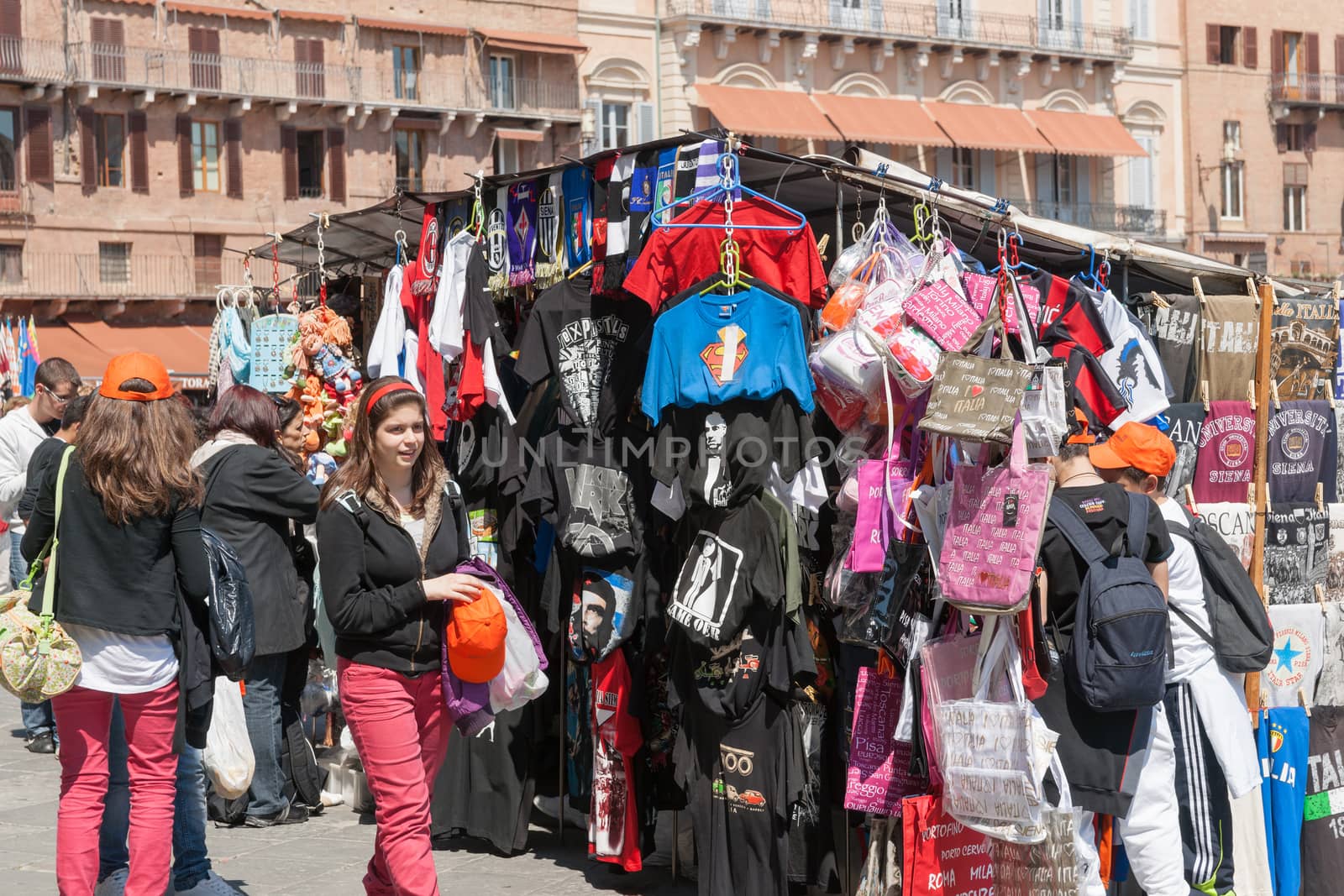 Siena, Italy - April 19, 2011: Tourists including two young woman both in pink trousers and black sweatshirts at market sales kiosk browsing and enjoying life in the Piazza Del Campo, Siena, Italy.