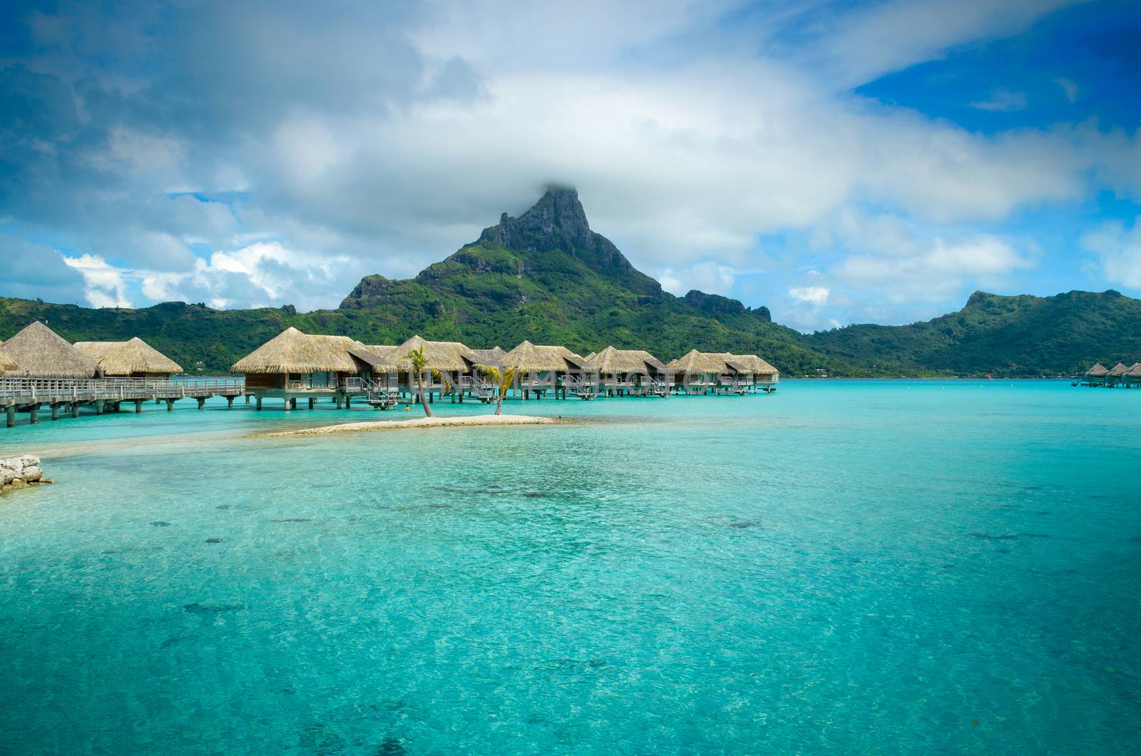 Luxury overwater thatched roof bungalow resort in a vacation resort in the clear blue lagoon with a view on the tropical island of Bora Bora, near Tahiti, in French Polynesia.