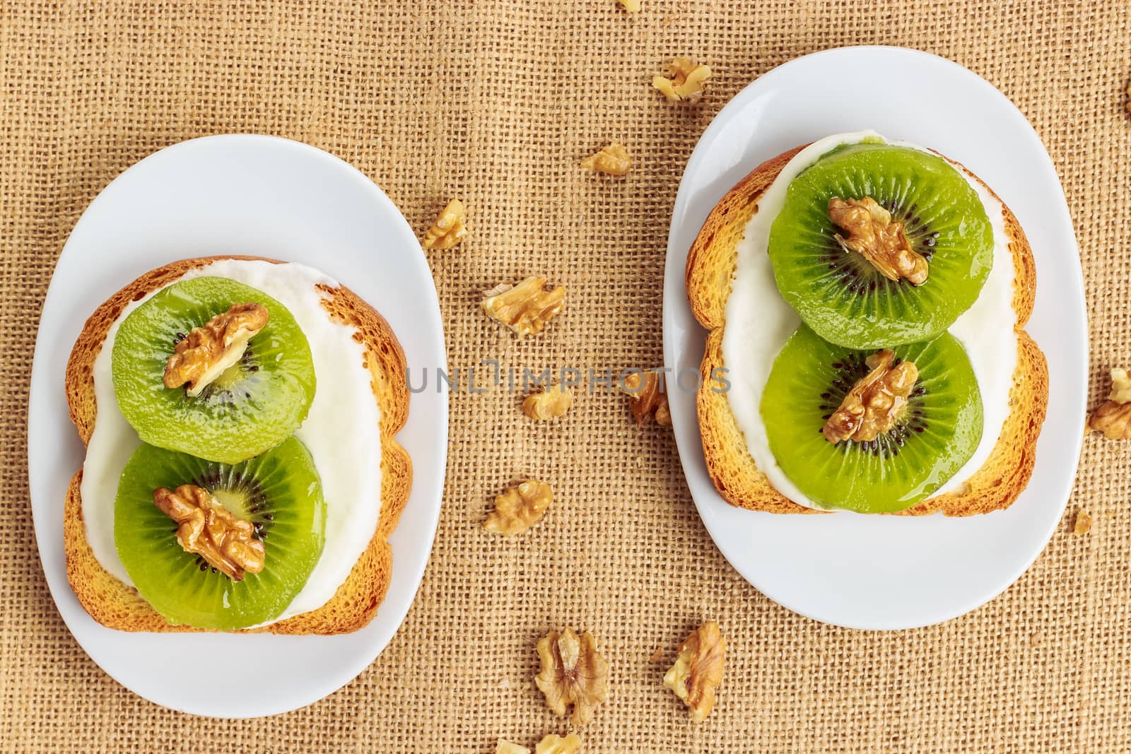 Toast with kiwi, cheese and walnuts on a piece of sackcloth with walnuts around. View from above 