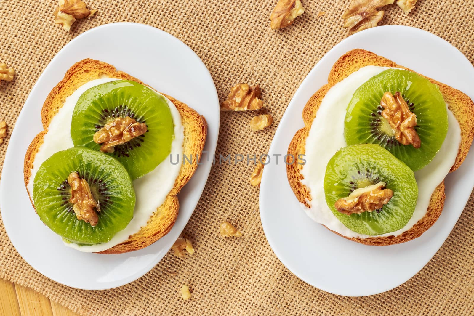 Toast with kiwi, cheese and walnuts on a piece of sackcloth with walnuts around. View from above 