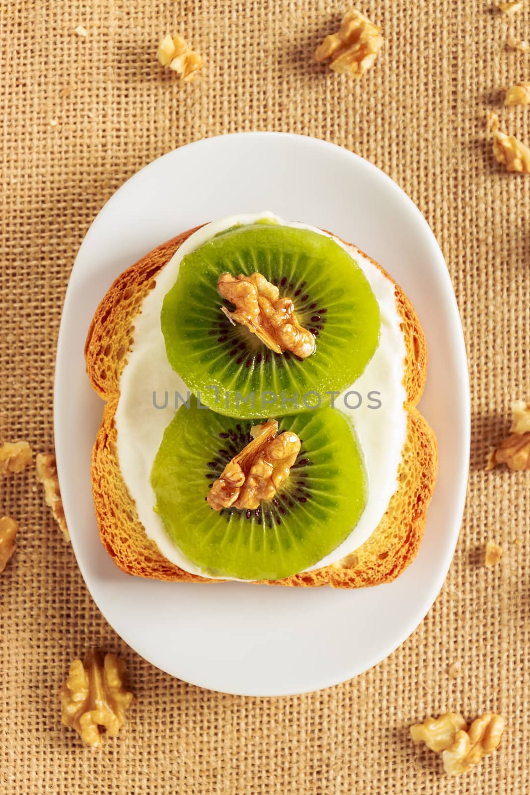 Toast with kiwi, cheese and walnuts on a piece of sackcloth with walnuts around. View from above 