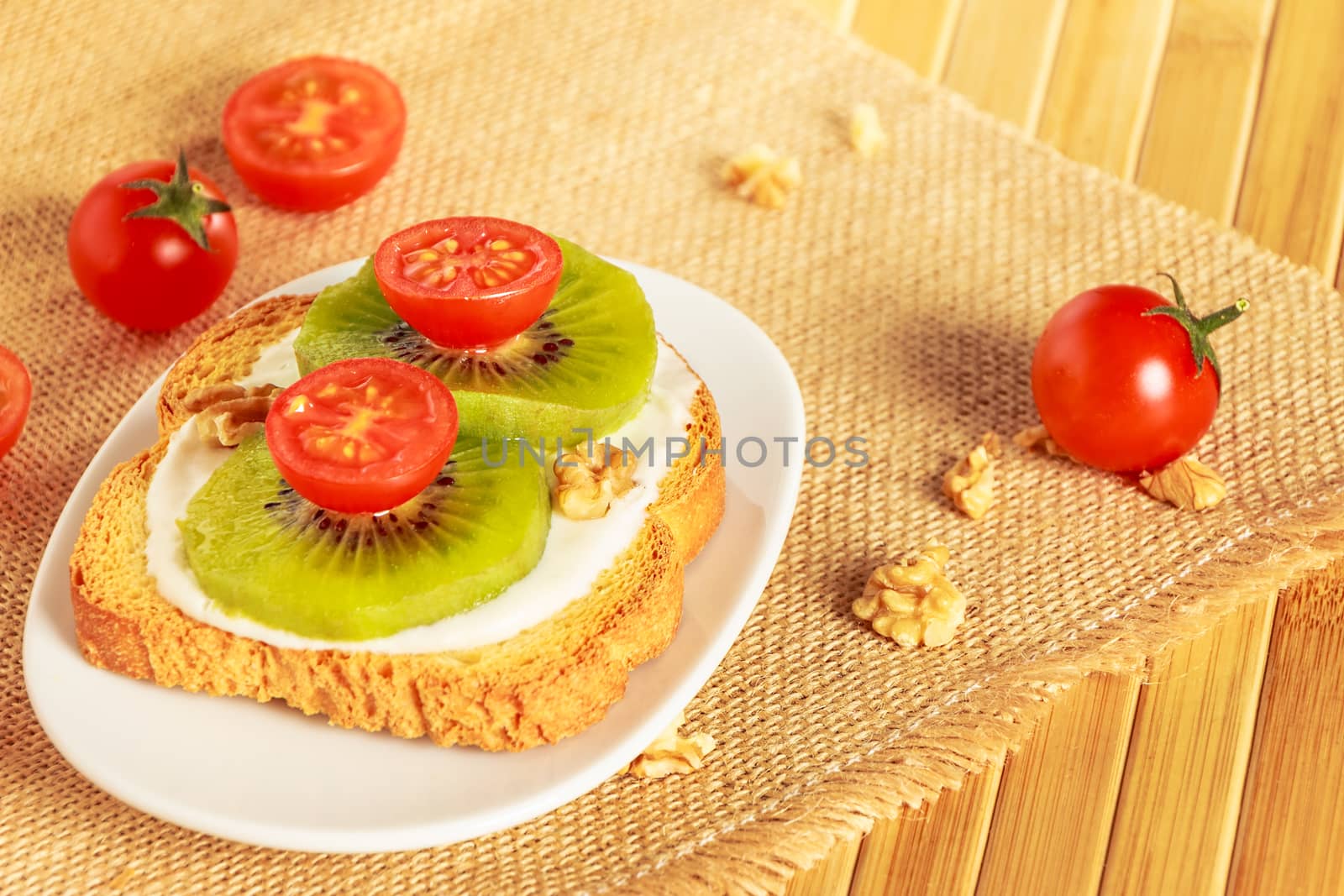 Toast with kiwi, cheese and cherry tomato on a piece of sackcloth in wooden board.