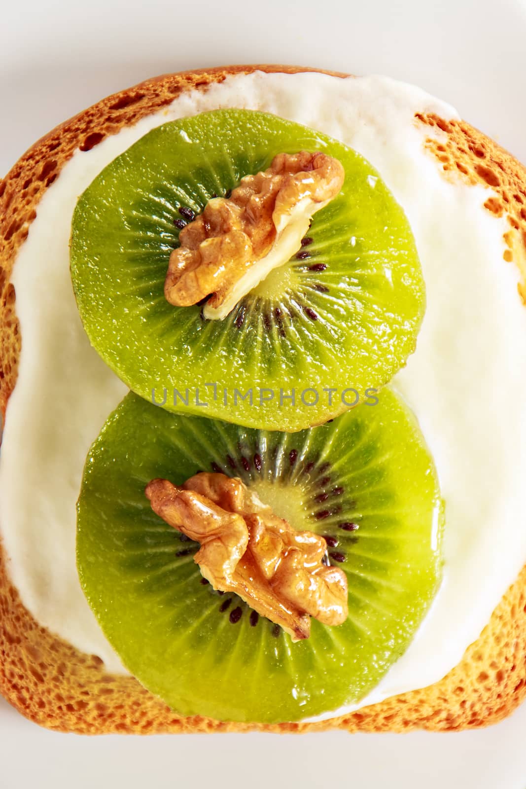 Toast with kiwi, cheese and walnuts on a white dish.View from above 