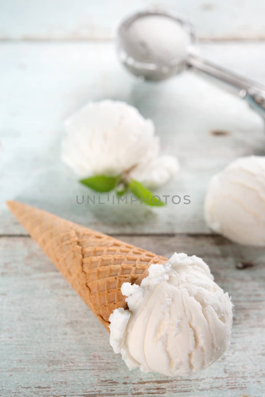 Scoop coconut ice cream in waffle cone with utensil on wood background.