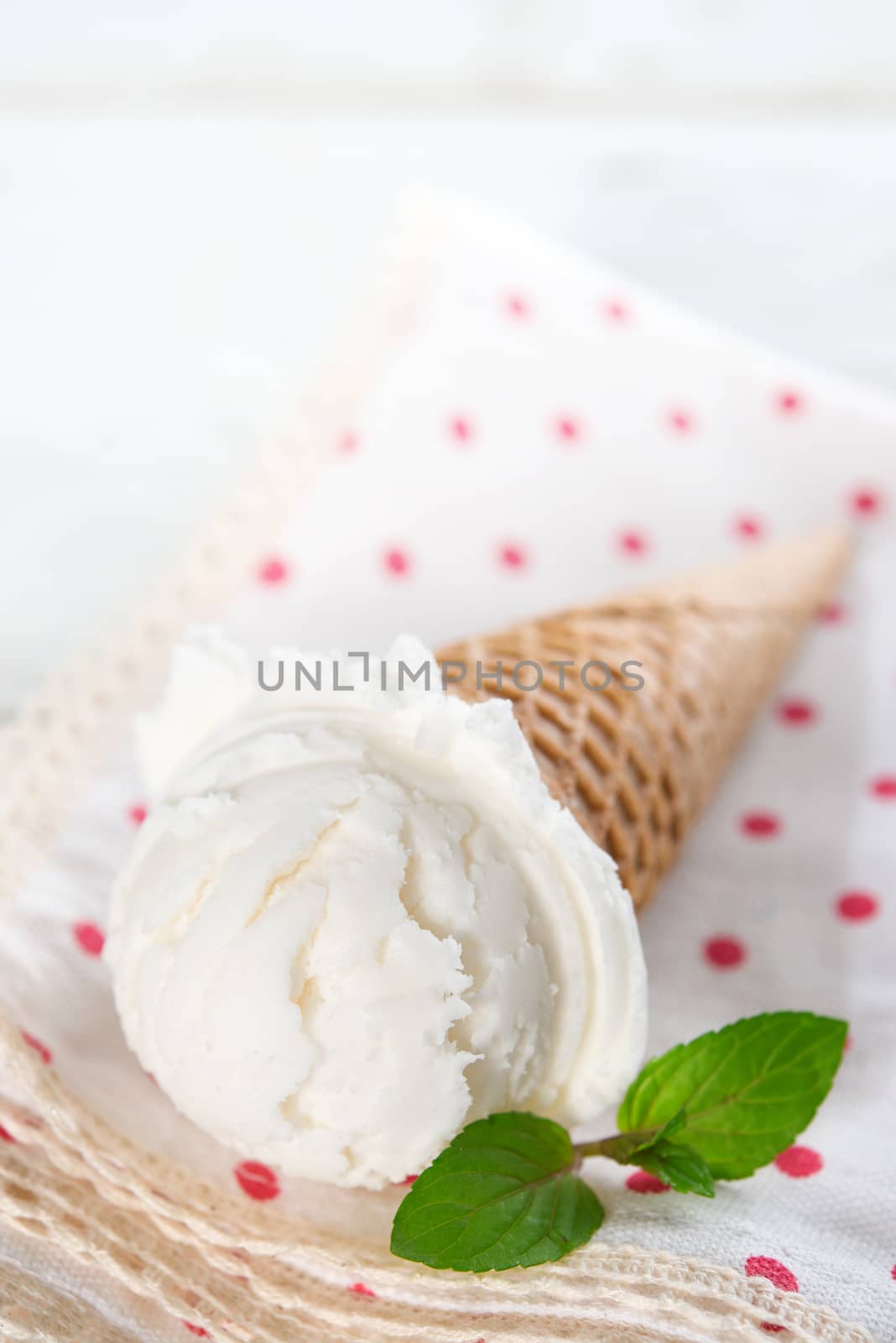 Scoop milk ice cream in waffle cone with mint on wood background.
