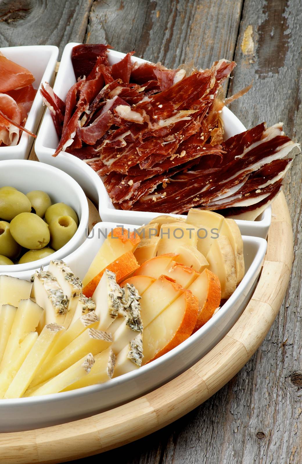 Various Spanish Snacks with Goat Cheeses, Jamon, Cured Ham and Green Olives on Serving Plate closeup on Wooden background