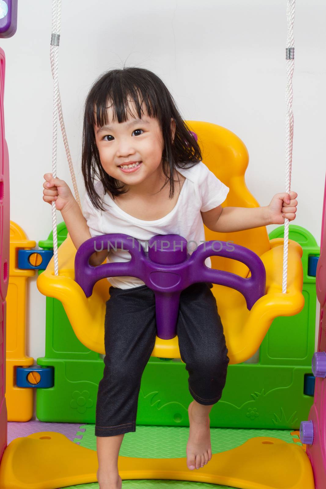 Asian Chinese children playing on swing at indoor playground.