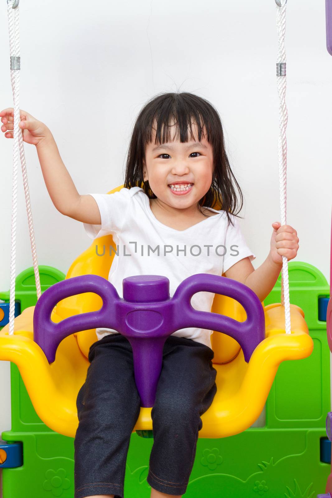 Asian Chinese children playing on swing at indoor playground.