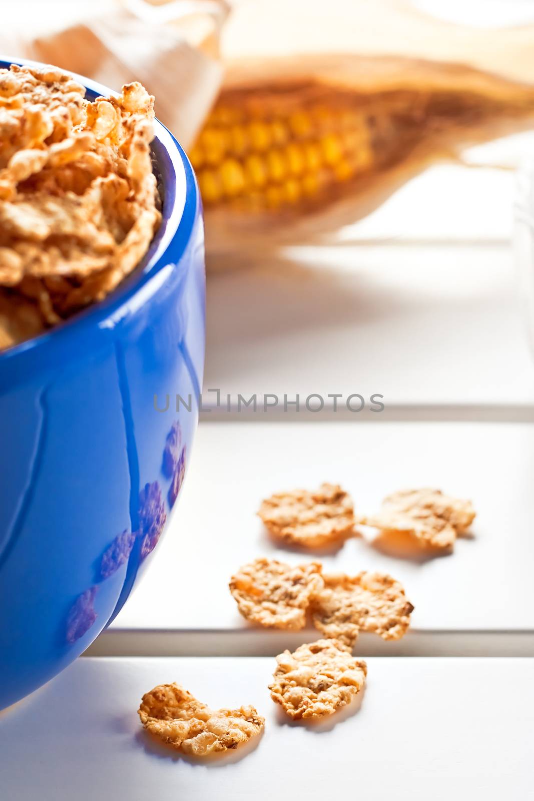 Cornflakes in a blue bowl on white wooden table with a cob