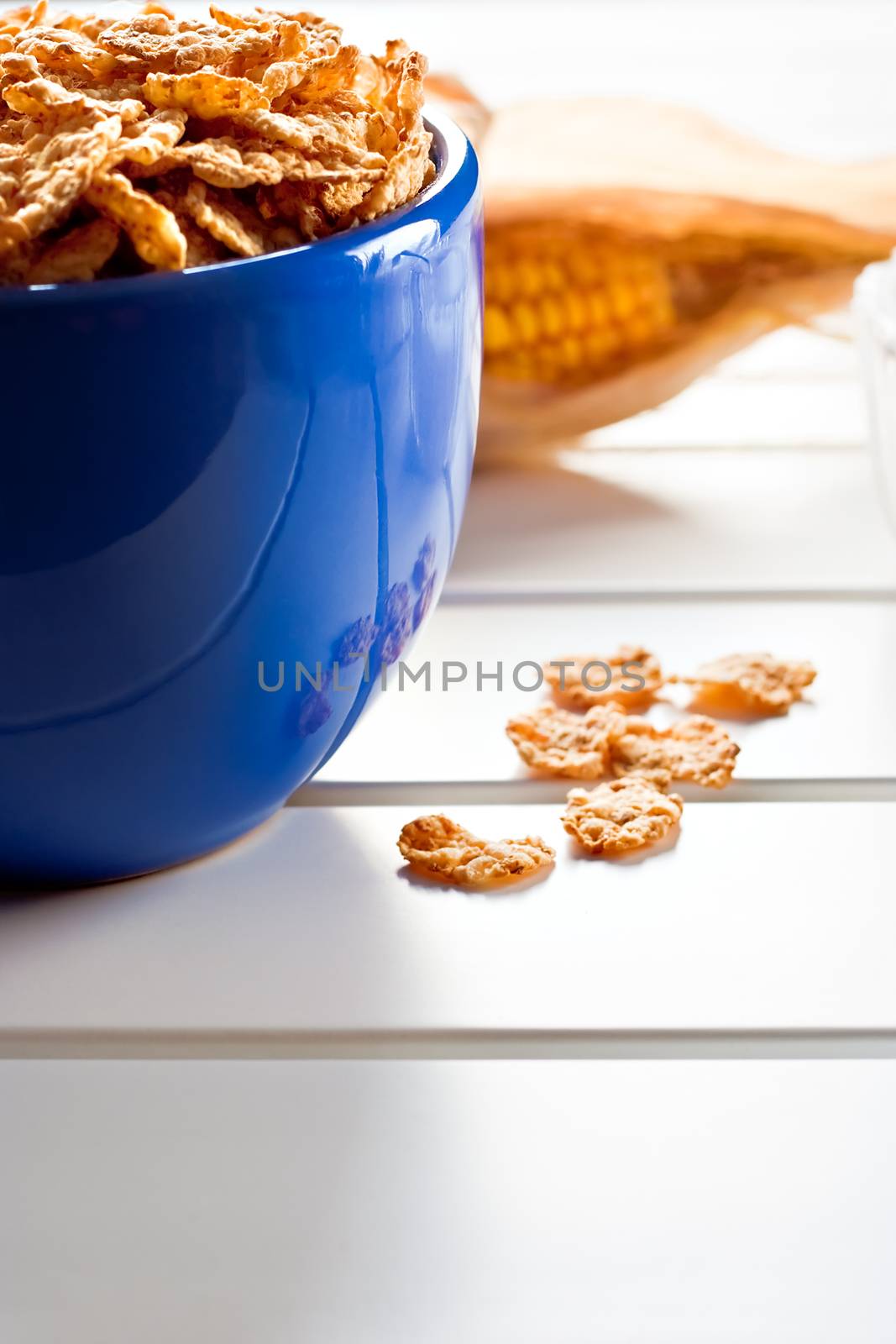 Cornflakes in a blue bowl on white wooden table with a cob