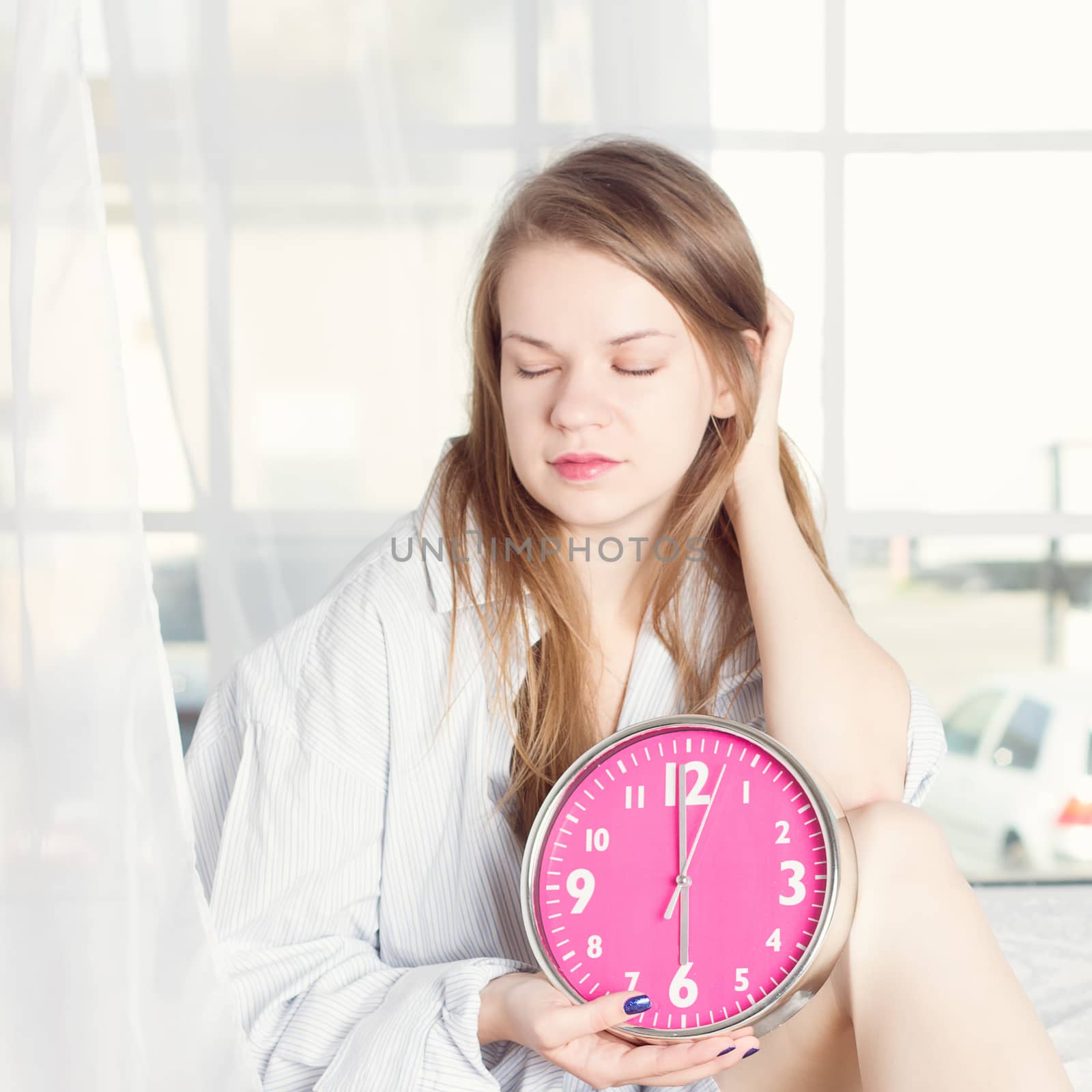 Young woman with alarmclock on the bed at the morning